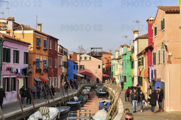 Strollers along the canal, typical street scene in winter, fishermen's houses in different colours, Burano, island in the lagoon of Venice, Italy