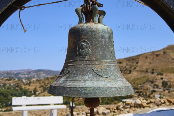 Antique metal bell in rural setting with background landscape and blue sky, Panagia tou Paleokastro, Church of the Old Fortress, Chapel, Panagia Kasteli, Lepides, Leros, Dodecanese, Greek Islands, Greece