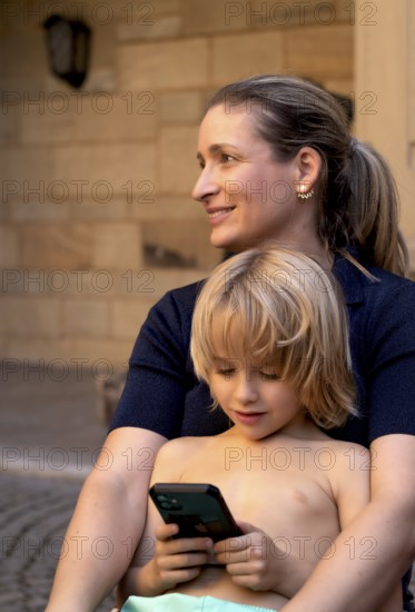 Mother, woman, has boy, 6 years, blonde, in arms, playing with smartphone, mobile phone, upper body naked, smiling, summer, Stuttgart, Baden-Württemberg, Germany