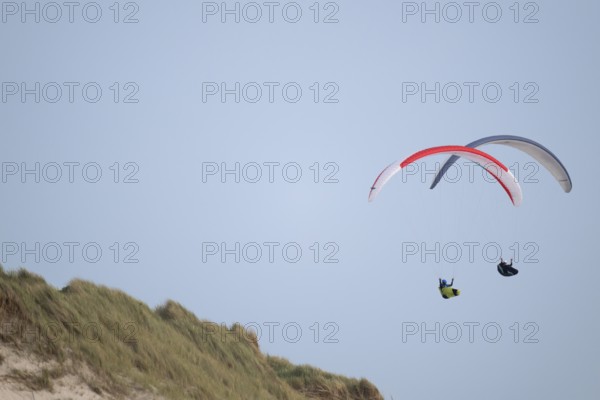 Two paragliders or paragliders in front of a blue sky over a dune landscape, near Hvide Sande, North Sea, Denmark