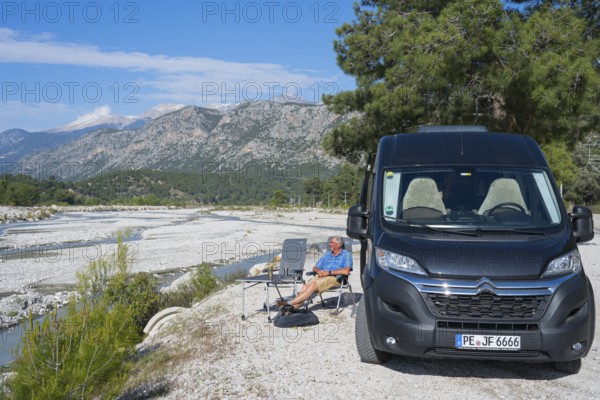 A man sits next to a motorhome on a riverbed surrounded by mountains, camper, Dargaz River near Saklikent, Saklikent, Antalya Province, Turkey