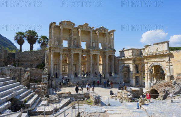 Ancient ruins with imposing columned facades and palm trees, surrounded by visitors under a blue sky, Celsus Library, on the right the south gate of the Agora, Efes, Ephesus, Ephesus, UNESCO World Heritage Site, Izmir Province, Ionia, Turkey