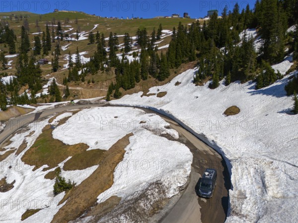 A winding road leads through a landscape of snow-covered hills and pine trees under a clear blue sky, aerial view, camper, motorhome, on the way to Goderdzi Pass, Adjara region, Adjara, autonomous republic, Georgia