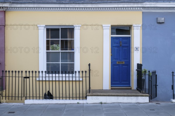 Colourful townhouse with blue door and yellow façade, surrounded by black fence, Kensington, London, England, United Kingdom