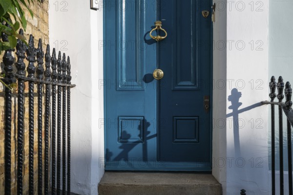 Blue door with brass-coloured door handle and wrought-iron grille in the sunlight, Kensington, London, England, Great Britain