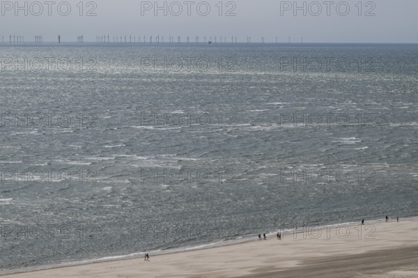 Wide sea view with sandy beach and pedestrians, wind turbines on the horizon, North Sea, Denmark