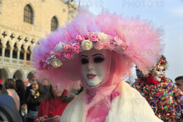 Venetian mask, disguised woman with big pink hat, walker, crowd on St Mark's Square, Carnival in Venice, Italy