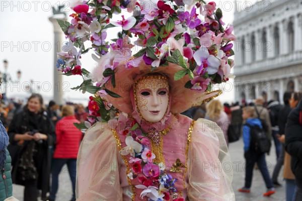 Venetian mask, disguised woman with big hat, walker, crowd on St Mark's Square, Carnival in Venice, Italy
