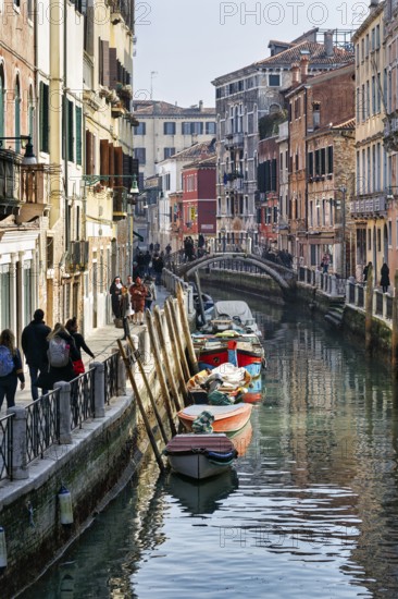 Walkers in winter, boats on canal, typical street scene in Venice, Italy