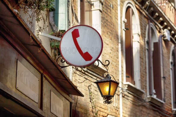 Sign with pictogram, red telephone receiver, public telephone, facade of a restaurant with street lamp, nostalgia, Venice, Italy