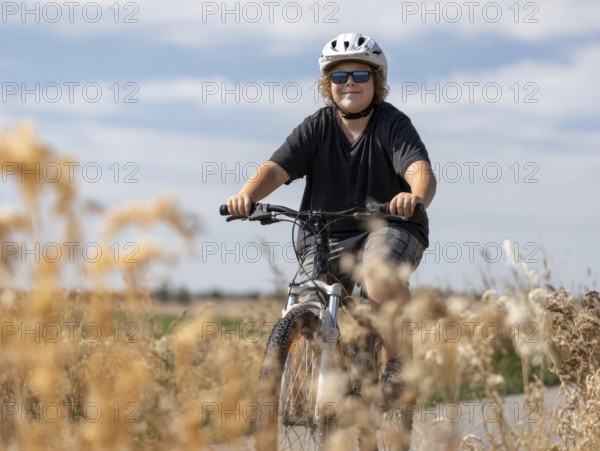 A boy with a bicycle helmet rides a bicycle and smiles friendly into the camera, AI generated, AI generated