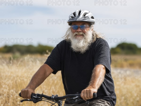 A man, senior citizen with a bicycle helmet rides on a bicycle and smiles friendly into the camera, AI generated, AI generated