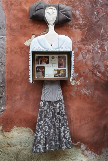 Abstract sculpture of a woman on a rust-red plastered wall. Figure holding a box with photos, vintage style, Eguisheim, Alsace, France