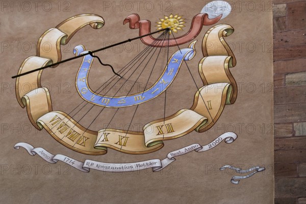 Artfully painted sundial on a sandstone wall with Roman numerals and decorative elements, Alsace, France