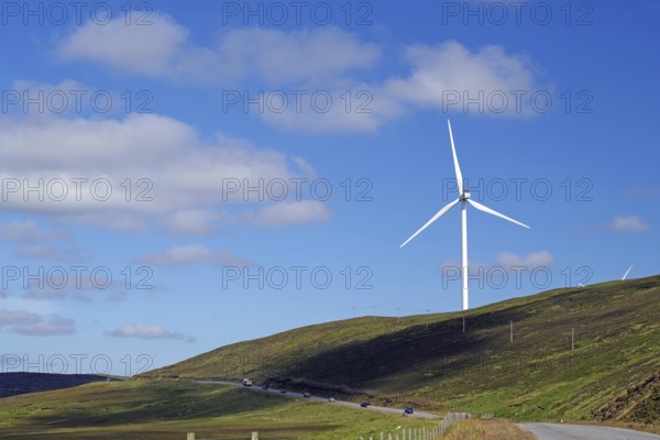 Single wind turbine on a hill next to a road under a blue sky, Mainland, Shetland Islands, Scotland, United Kingdom