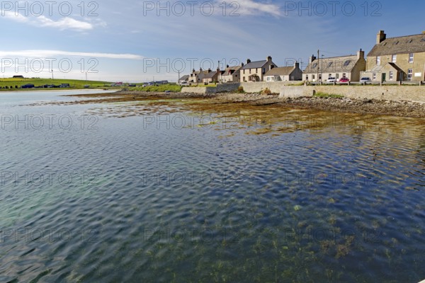 Quiet coastal village with houses along the water and blue sky in the background