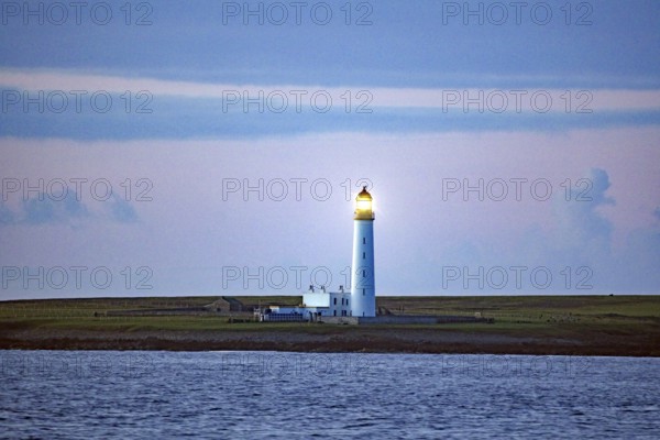 Lighthouse on the coast at dusk with blue sky in the background, crossing between Orkney and Shetland Islands, Scotland, Great Britain