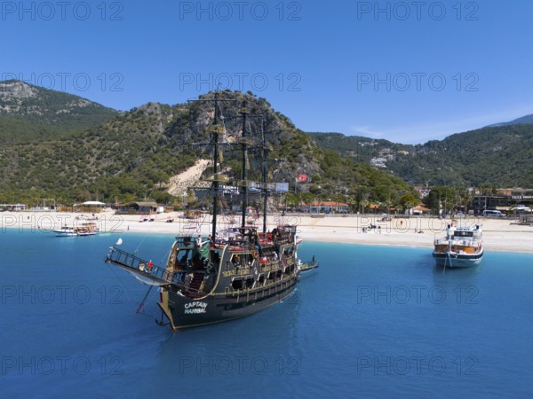 Pirate ship sails in front of a picturesque coastal landscape with mountains and clear blue water, aerial view, Fethiye, Mugla, Mugla, Aegean Sea, Turkey