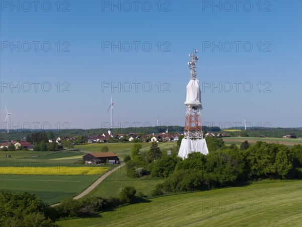 A transmission tower and wind turbines near a village under a blue sky, radio tower being renovated, near Hohenstadt, Swabian Alb, Baden-Württemberg, Germany