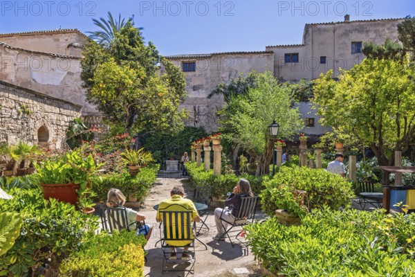 People sitting on chairs and enjoying the sun in the botanical garden at The Arab baths in Palma, Palma de Mallorca, Mallorca, Spain