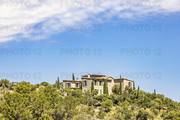 House on a hill with lush green trees and a sunny blue sky in the summer, Mallorca, Spain