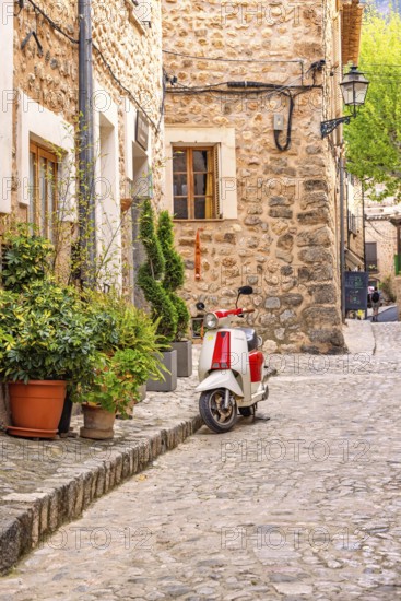 Scooter standing outside a house on the city street with lush green plants in pots on the pavement in an idyllic spanish village, Sóller, Mallorca, Spain