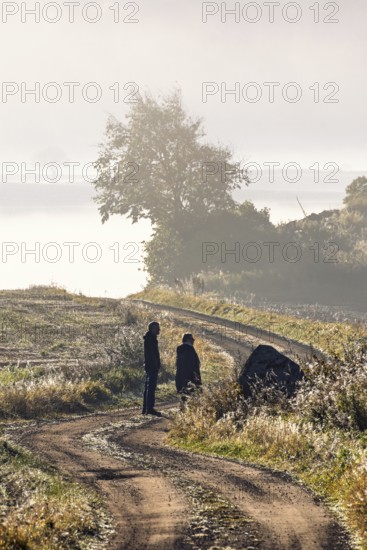 Two people walking on a winding gravel road in the countryside on a foggy autumn day