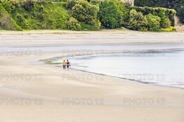 Two people walking at the waters edge on a sandy beach by the sea, Morgat, Crozon peninsula, Bretagne, France