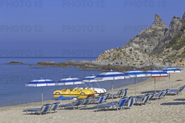 Beach with sunbeds and parasols in front of a rocky coast and blue sky, Ricadi, Capo Vaticano