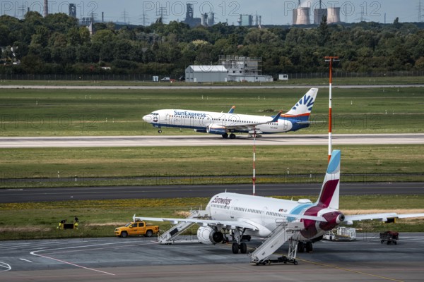 Düsseldorf Airport, Eurowings Airbus aircraft on the apron, SunExpress Boeing 737-800 taking off, in the background the HKM steelworks in Duisburg, North Rhine-Westphalia, Germany