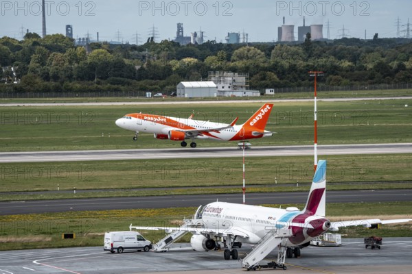 Düsseldorf Airport, Eurowings Airbus aircraft on the apron, EasyJet Airbus A320-200 taking off, in the background the HKM steelworks in Duisburg, North Rhine-Westphalia, Germany