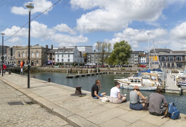 People sitting on quayside of marina harbour, The Barbican, Plymouth, Devon, England, UK