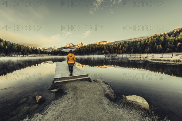 Young woman at Lake Staz near Sankt Moritz in the Engadine in Switzerland. Morning atmosphere with fog in autumn. Reflection of water