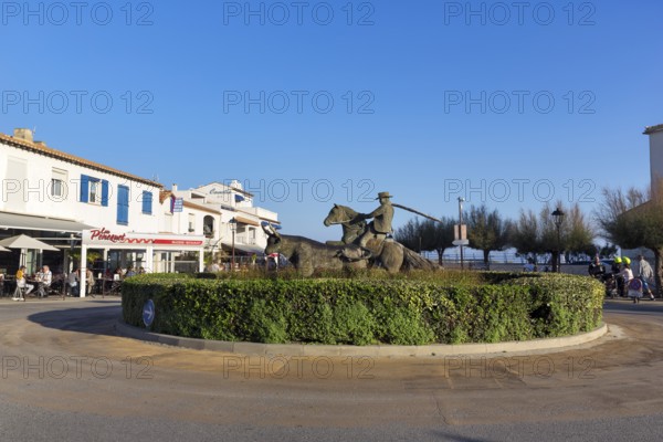 Roundabout with sculptures, cattle herder, guardian of the Camargue on a horse, next to a bull, Saintes-Maries-de-la-Mer, Camargue, France