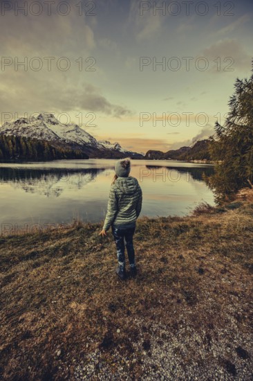 Woman by the lake in autumn Engadine in Switzerland with snow-covered mountain peaks