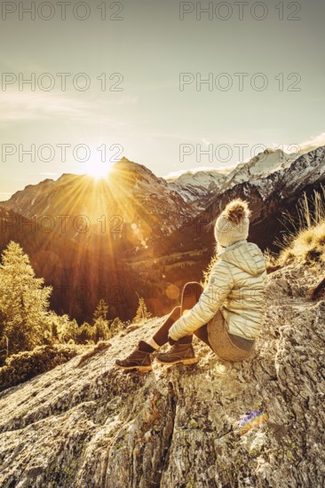 Woman sitting thoughtfully at a feslen at autumn atmosphere during sunset in the Swiss Alps in the Engadine. Photographed from the village of Maloja on the Maloja Pass