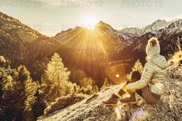 Woman sitting thoughtfully at a feslen at autumn atmosphere during sunset in the Swiss Alps in the Engadine. Photographed from the village of Maloja on the Maloja Pass