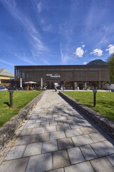 AlpenCongress Berchtesgaden, congress hall, modern architecture, building, outdoor area of a restaurant with parasols, lawn, footpath, paving slabs, lamp, blue sky, cumulus clouds, cirrostratus clouds, Maximilianstraße, Berchtesgaden, Upper Bavaria, district of Berchtesgadener Land, Bavaria, Germany