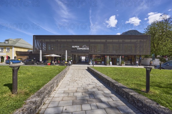 AlpenCongress Berchtesgaden, congress hall, modern architecture, building, outdoor area of a restaurant with sunshades, lawn, footpath, pavement slabs, lamp, trees, blue sky, cumulus clouds, cirrostratus clouds, Maximilianstraße, Berchtesgaden, Upper Bavaria, district Berchtesgadener Land, Bavaria, Germany