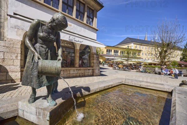 Mother-child fountain, fountain with bronze sculptures, sculptor Fritz Schelle, square, pedestrian zone, outdoor area of a restaurant with parasols, visitors as secondary motif, general architecture, fashion shop, retail trade, blue sky, cirrostratus clouds, market square, Metzgerstraße, Berchtesgaden, Upper Bavaria, district of Berchtesgadener Land, Bavaria, Germany