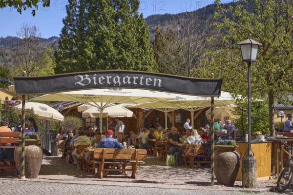 Beer garden, entrance, outdoor area of a restaurant with parasols, tables and benches, lantern, trees, mountains, forest, visitors as secondary motif, blue sky, cloudless, market square, Berchtesgaden, Upper Bavaria, Berchtesgadener Land district, Bavaria, Germany