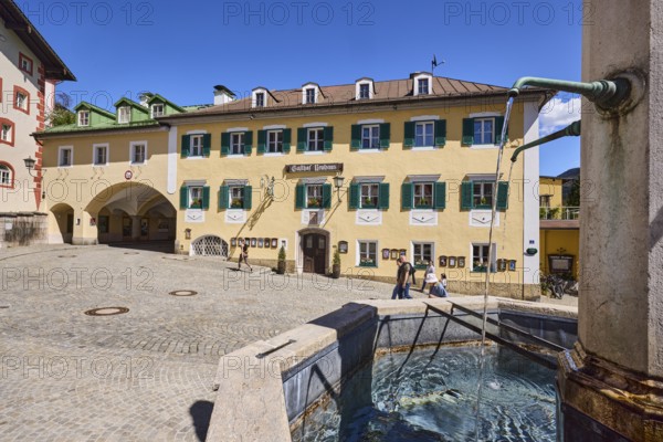Market fountain, Gasthof Neuhaus, stone fountain, historical buildings, pedestrian zone, square, cobblestones, archway, pedestrians as secondary motif, blue sky, cloudless, market square, Berchtesgaden, Upper Bavaria, Berchtesgadener Land district, Bavaria, Germany