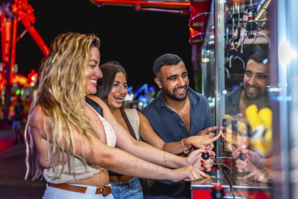 Happy friends enjoying a night out at amusement park, playing skill crane game and trying to win a prize