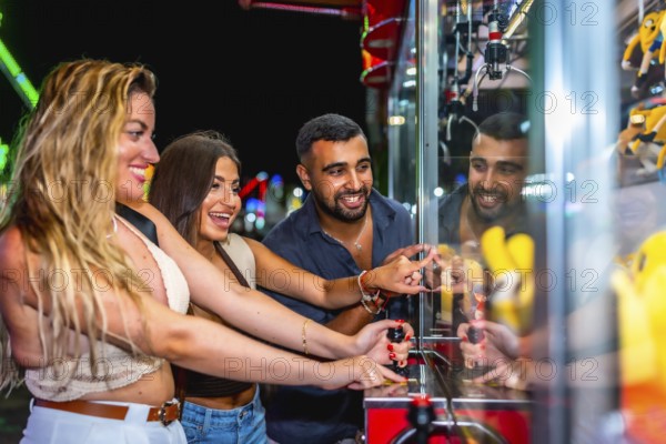 Group of friends having fun playing a crane game, trying to grab a prize, at an amusement park at night
