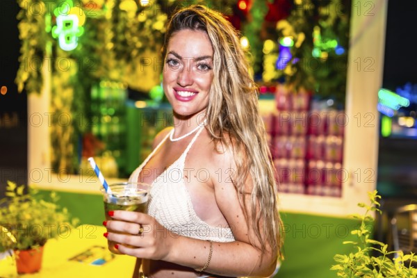 Young woman smiling and holding a refreshing cocktail at a vibrant night market, enjoying the festive atmosphere