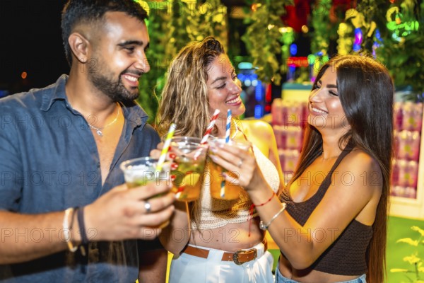 Happy friends enjoying drinks at open air bar, celebrating togetherness with cocktails under night lights