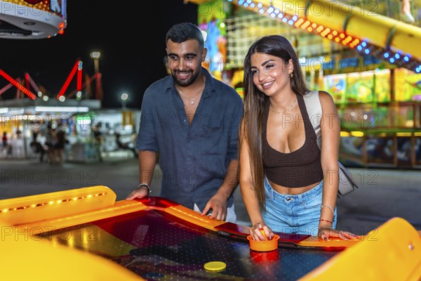 Happy young couple enjoying a lively night out, playing air hockey together at a colorful amusement park filled with excitement and joy