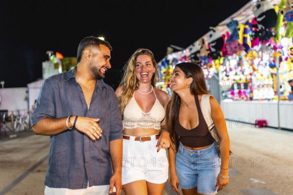 Group of three young friends laughing and walking together in an amusement park, enjoying the vibrant lights and festive atmosphere of the night