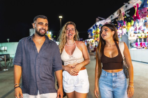 Three friends are enjoying their time together, strolling through a vibrant amusement park at night