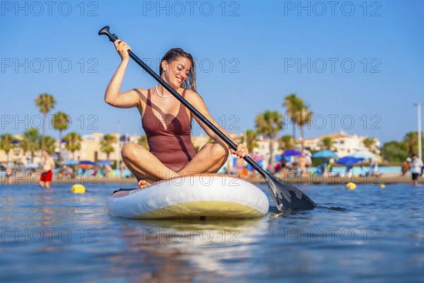 Smiling woman paddling on a stand up paddle board on a sunny summer day at the beach, enjoying her vacation